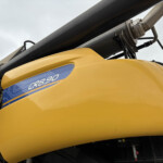 Close-up of yellow heavy equipment with a blue CR8.90 badge and a large black cylindrical boom above it