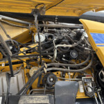 Interior view of a yellow agricultural machine showing belts, pulleys, hoses and metal framework
