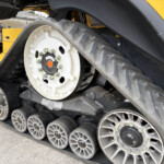 Close-up of a large wheel and rubber track on a yellow tracked construction machine, with bolts and metal components visible in the foreground.