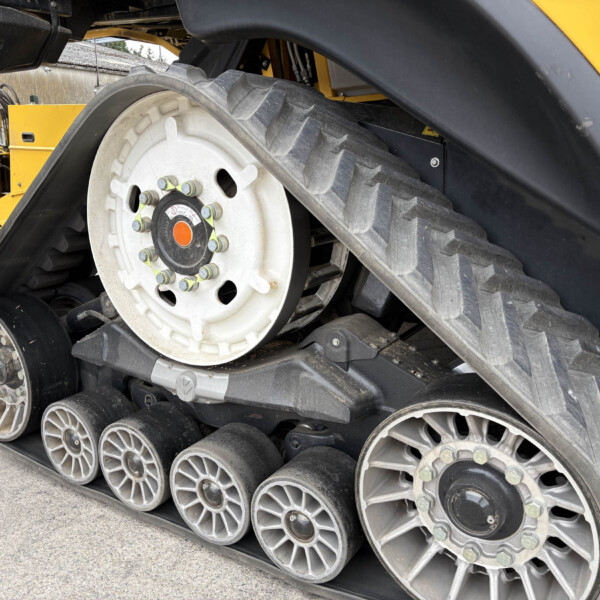 Close-up of a large wheel and rubber track on a yellow tracked construction machine, with bolts and metal components visible in the foreground.