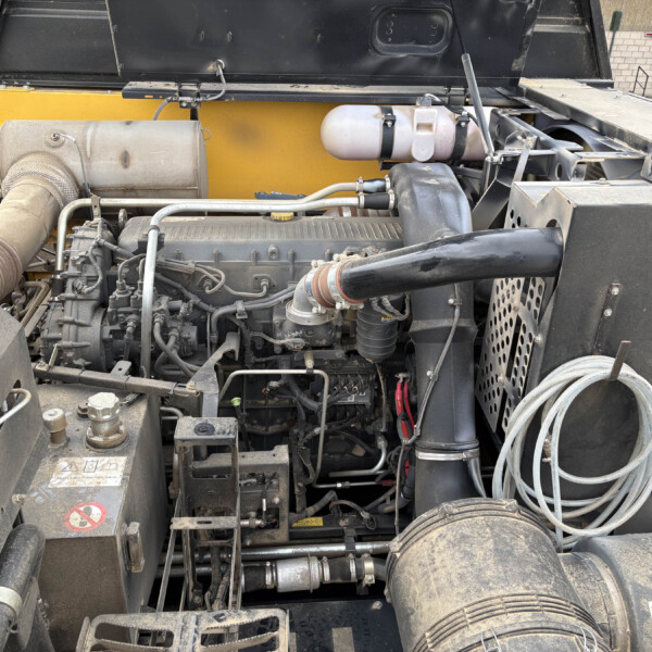 Engine compartment of a heavy-duty vehicle, showing hoses, belts, and wiring with a dusty, black and yellow chassis in view.