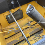 Close-up of a yellow industrial machine interior featuring a dusty metal chute and supporting rods, viewed at an angle.