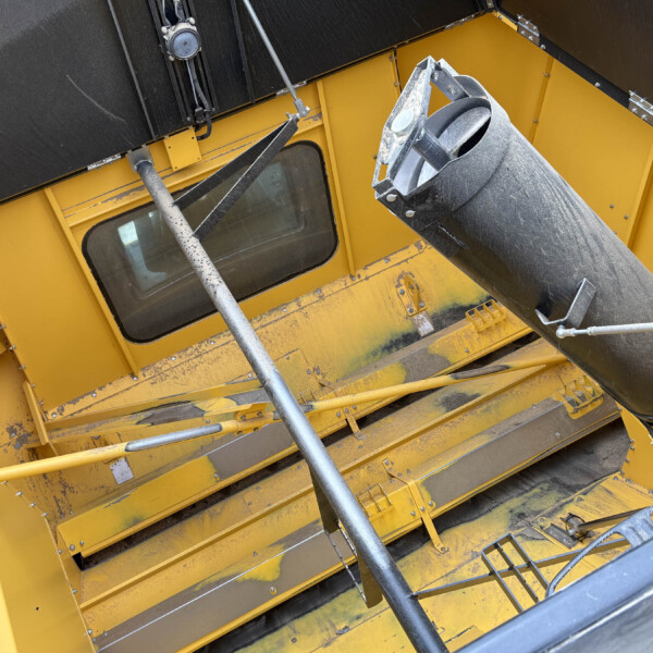 Close-up of a yellow industrial machine interior featuring a dusty metal chute and supporting rods, viewed at an angle.
