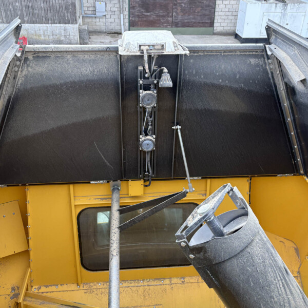 Interior of a dusty yellow dump truck bed with black side walls and a central hydraulic chute mechanism at the top.