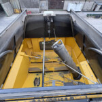 Interior of a large industrial hopper/dump bed: yellow steel frame, black sidewalls, dusty surfaces and central pipe assembly visible from above.