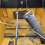 Industrial machinery interior with yellow steel framework and a large black inclined chute or duct at center.