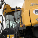 Close-up of a yellow construction excavator cab with safety decals and brand logos (Twin Rotor, Russell's).