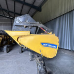 Yellow New Holland farming machine parked inside a metal shed, logo visible on the side panel.