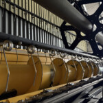 Close-up of an industrial machine showing a yellow support beam, a row of spiral springs along a black rail, and a dark blue structural frame in the background.