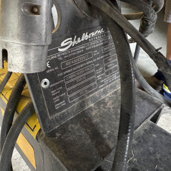 Close-up of a black machinery plate with Shelbourne Reynolds branding, showing serial numbers and weight details amid wires and hoses.