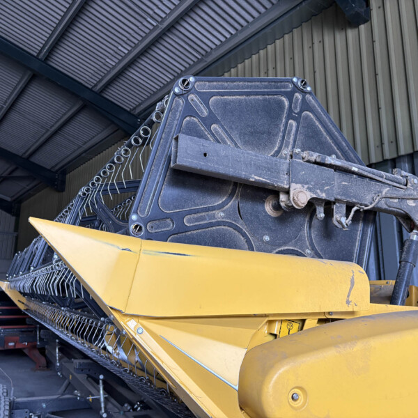 Large yellow industrial conveyor/harvester inside a workshop, with metal framework and cables visible around it.