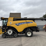 Side view of a yellow New Holland CR8.90 combine harvester with a large unloading auger, parked in a paved lot under a cloudy sky.