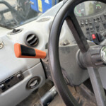 Inside a tractor cab: steering wheel, dashboard controls, and an orange hand lever near the dashboard.
