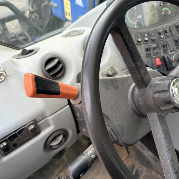 Inside a tractor cab: steering wheel, dashboard controls, and an orange hand lever near the dashboard.