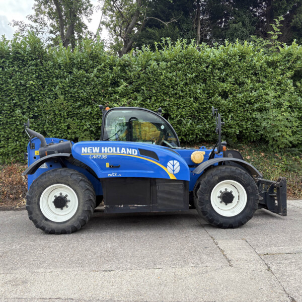 Blue New Holland compact tractor parked on a paved surface with a dense green hedge behind it, outdoors.