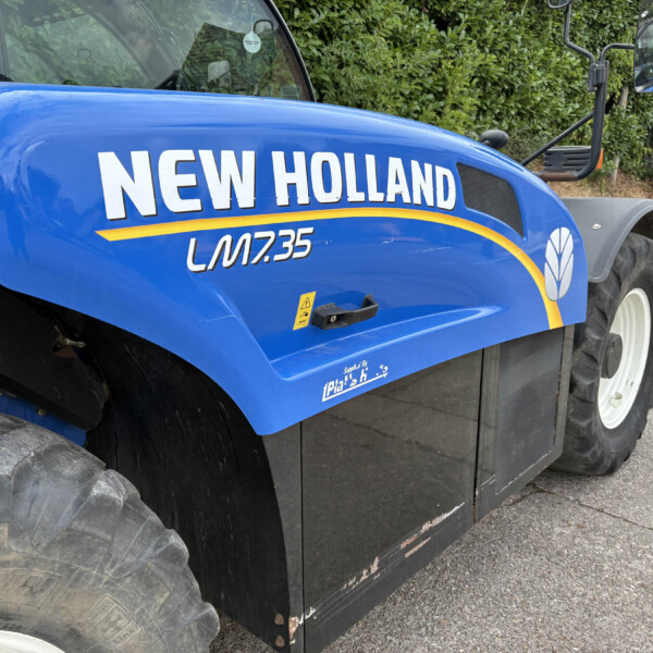 Close-up of a blue New Holland tractor with the bold white 'NEW HOLLAND' logo and a yellow stripe along the side.