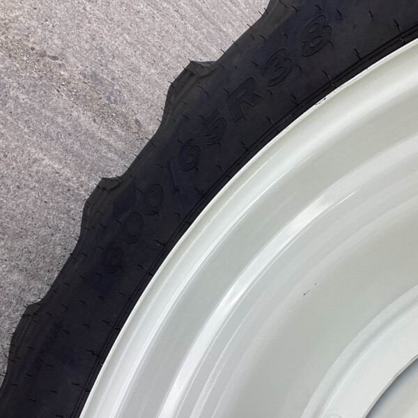 Close-up of a black tire with visible tread next to a light-colored metal rim on rough pavement surface.