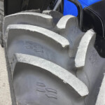 Close-up of large black rubber tracks with chevron tread on a heavy machine, blue body panel visible in the background.