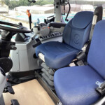 Cockpit of a heavy construction vehicle showing a steering wheel, blue seats, and control panel with levers and pedals.
