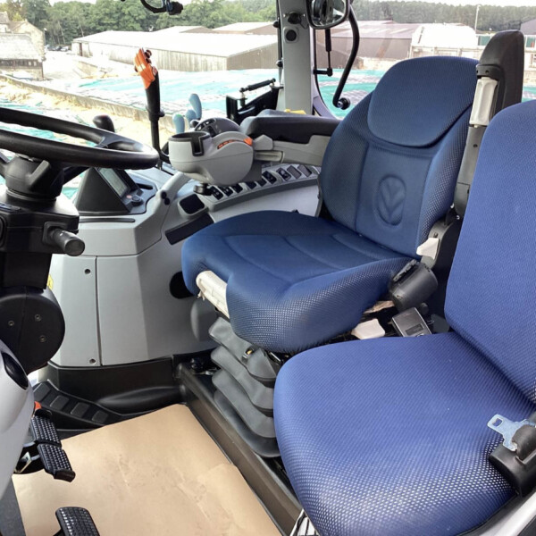 Cockpit of a heavy construction vehicle showing a steering wheel, blue seats, and control panel with levers and pedals.