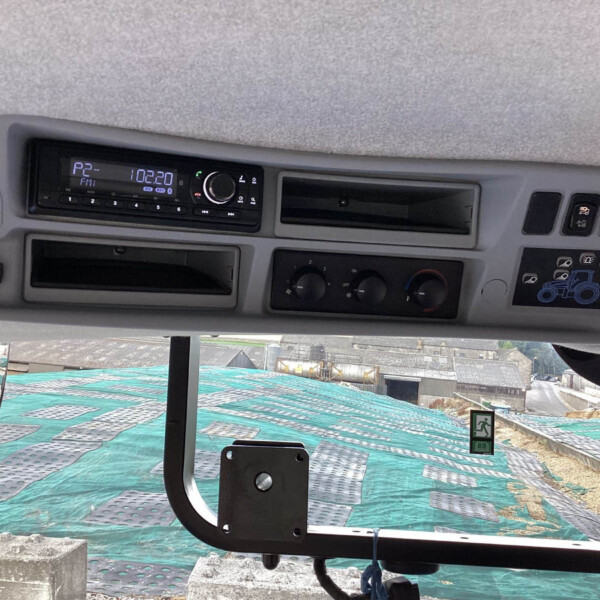 Interior of a vehicle cab with a radio display reading 102.20 FM and climate/control buttons visible; construction site outside the windshield.