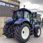 Front-right view of a large blue tractor with oversized white wheels parked outside a workshop, sign reading 'RUSSELLS' on the wall behind it.