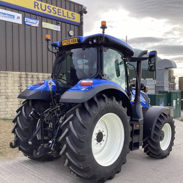 Front-right view of a large blue tractor with oversized white wheels parked outside a workshop, sign reading 'RUSSELLS' on the wall behind it.