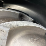 Close-up of stacked tires with small metal studs, showing a torn edge of a tire guard inside a dark wheel well.