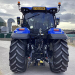 Rear view of a blue agricultural tractor with oversized rear tires and orange warning beacons in a yard. License plate FY25 VBA is visible on the cab roof.