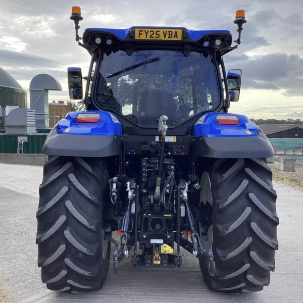 Rear view of a blue agricultural tractor with oversized rear tires and orange warning beacons in a yard. License plate FY25 VBA is visible on the cab roof.