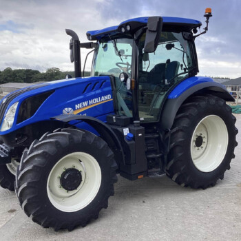 Blue New Holland tractor parked on a construction site, close-up of the front and large tires with a cloudy sky in the background