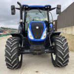 Front view of a large blue tractor with oversized treaded tires in a yard, facing the camera.