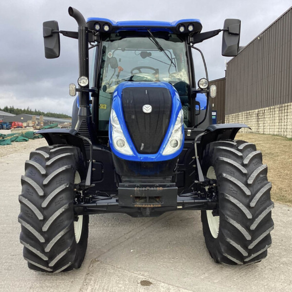 Front view of a large blue tractor with oversized treaded tires in a yard, facing the camera.