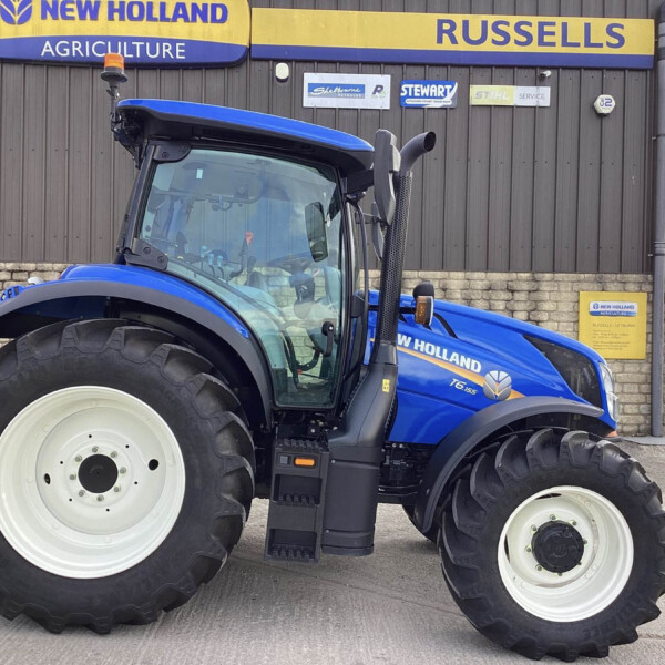 Blue New Holland tractor with oversized front tires parked in front of a building displaying New Holland Agriculture signage.