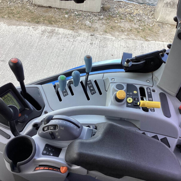 Interior view of a blue tractor cab with multiple control levers, joysticks, and dashboard buttons within reach of the driver.