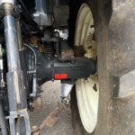 Close-up of a tractor's front hydraulic system and hitch, with rusted metal brackets and a large treaded tire nearby.