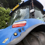 Close-up of a blue tractor cab with a large front tire and visible warning stickers on the body.