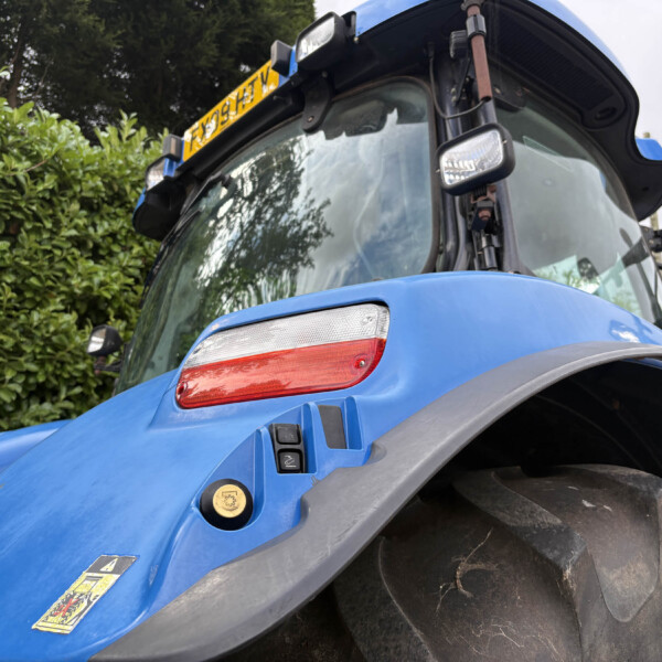 Close-up of a blue tractor cab with a large front tire and visible warning stickers on the body.