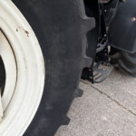 Close-up of a large white wheel rim and black treaded tractor tire on a paved surface with rust spots nearby.