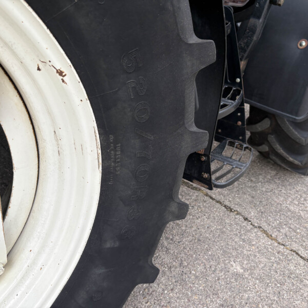 Close-up of a large white wheel rim and black treaded tractor tire on a paved surface with rust spots nearby.