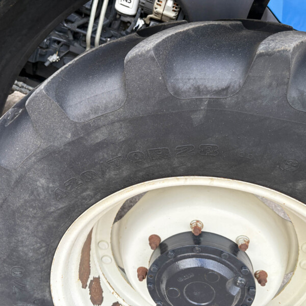 Close-up of a large tractor tire with a white rim, showing dirt, rust, and worn tread details.