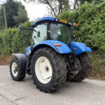 Blue tractor parked outdoors with large white-rimmed rear wheels, hedge backdrop and a yellow license plate FX09 HTV in view.