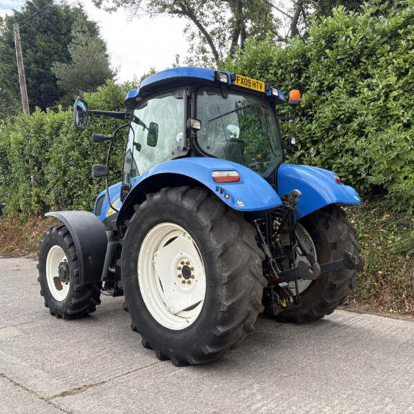 Blue tractor parked outdoors with large white-rimmed rear wheels, hedge backdrop and a yellow license plate FX09 HTV in view.