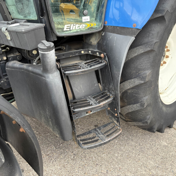 Close-up of a blue tractor with black steps and a large treaded tire, showing the Elite logo on the cab window.