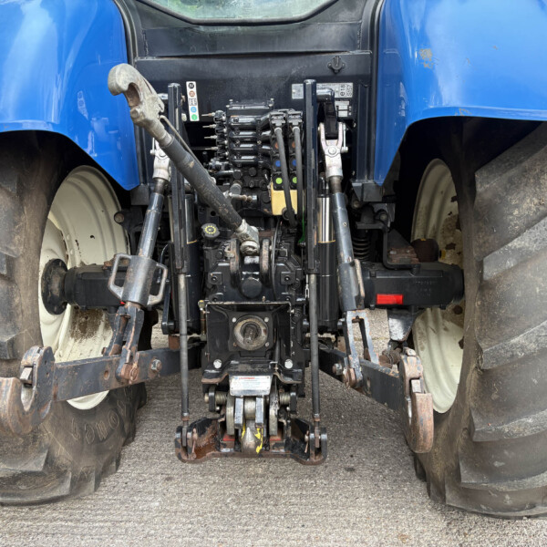 Rear view of a blue tractor showing the hydraulic three-point hitch and power take-off area between large muddy tires.