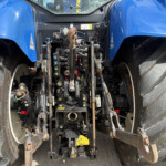 Rear view of a blue tractor showing its hydraulic three-point hitch and control levers between large tires.