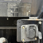 Close-up of a dusty vehicle data plate with specifications and weights, mounted on a metal surface near a latch and bolts.