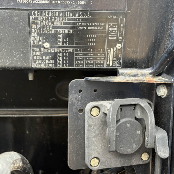 Close-up of a dusty vehicle data plate with specifications and weights, mounted on a metal surface near a latch and bolts.