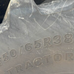 Close-up of a dark, scratched metal surface with raised alphanumeric characters (shows '65R38') part of a vehicle or equipment plate.