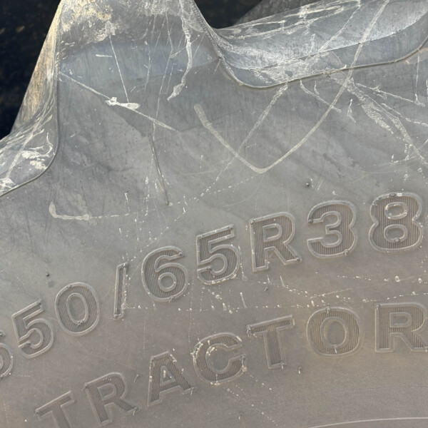 Close-up of a dark, scratched metal surface with raised alphanumeric characters (shows '65R38') part of a vehicle or equipment plate.